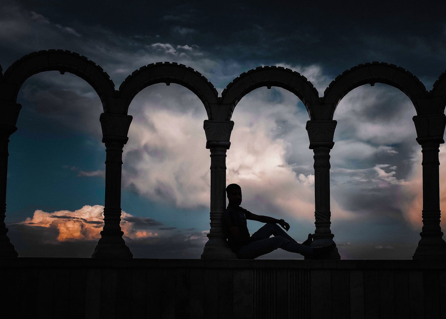 silhouette photo of person leaning on arch pillar